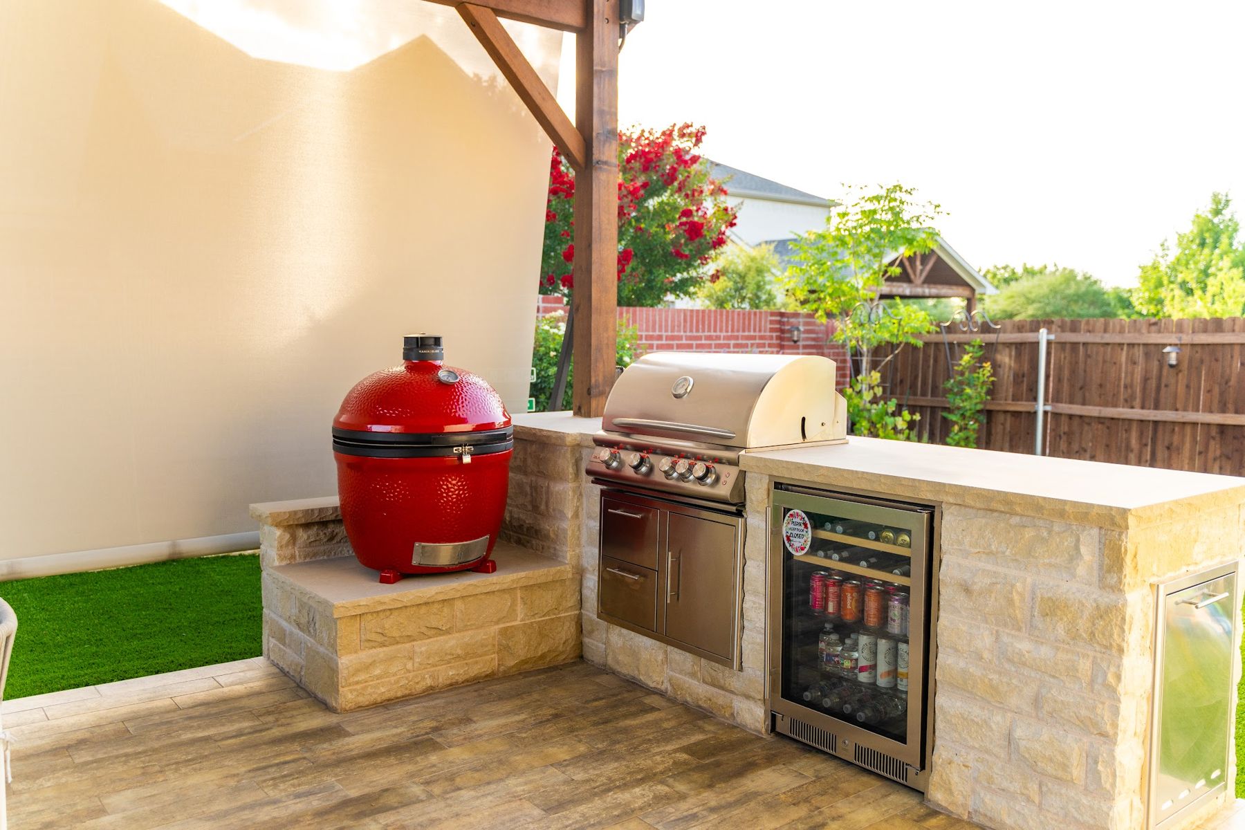 Outdoor kitchen with built-in grill, red kamado cooker and beverage fridge in a limestone island, Aledo