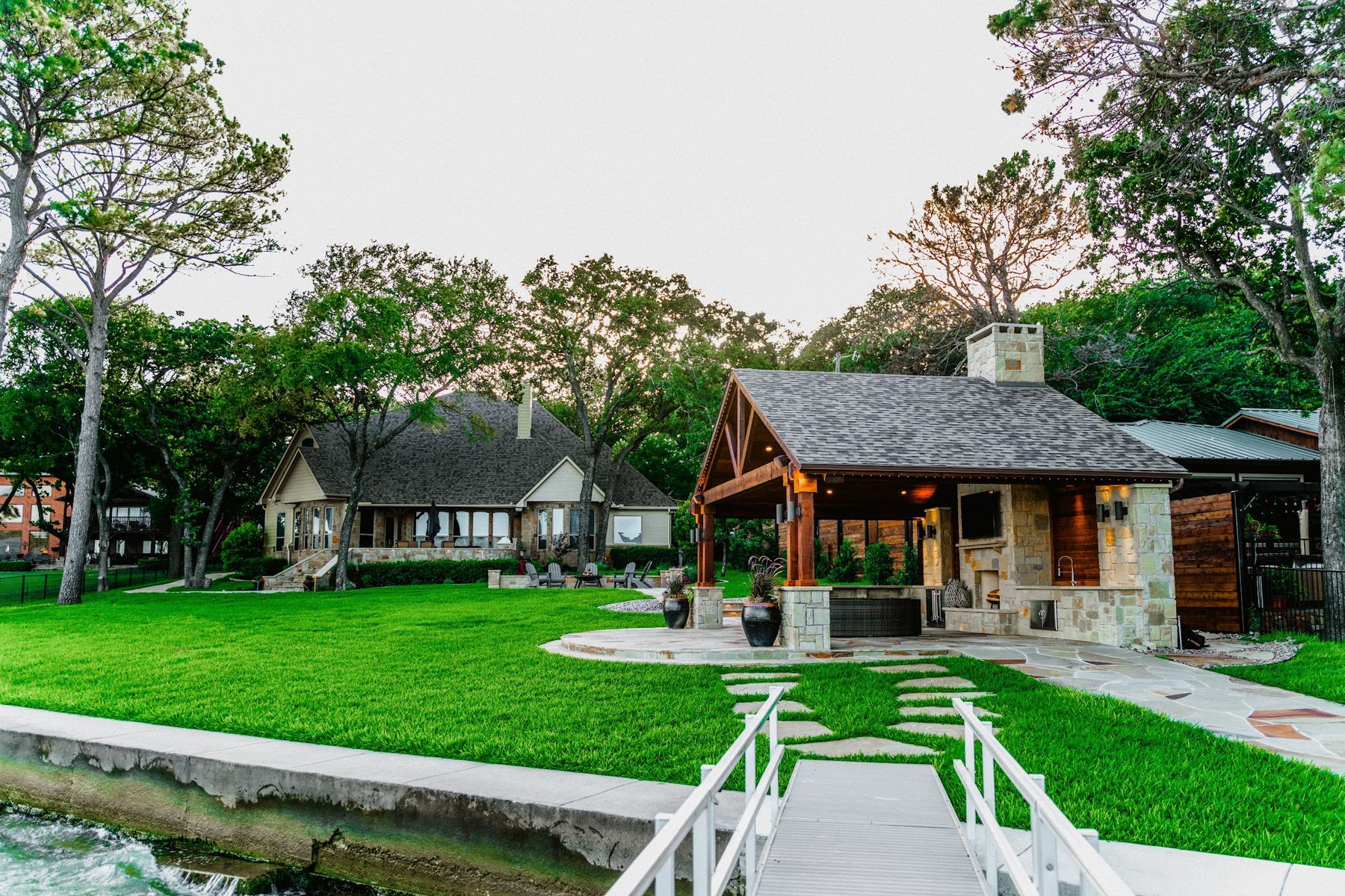 Timber pavilion and stone chimney on a lakefront lawn with a footbridge, Eagle Mountain Lake