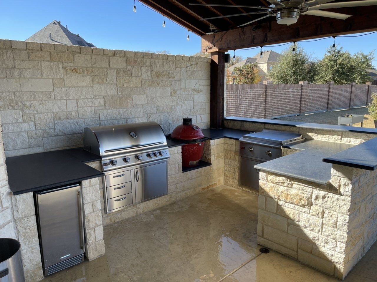 L-shaped limestone kitchen with grill, red kamado and beverage fridge