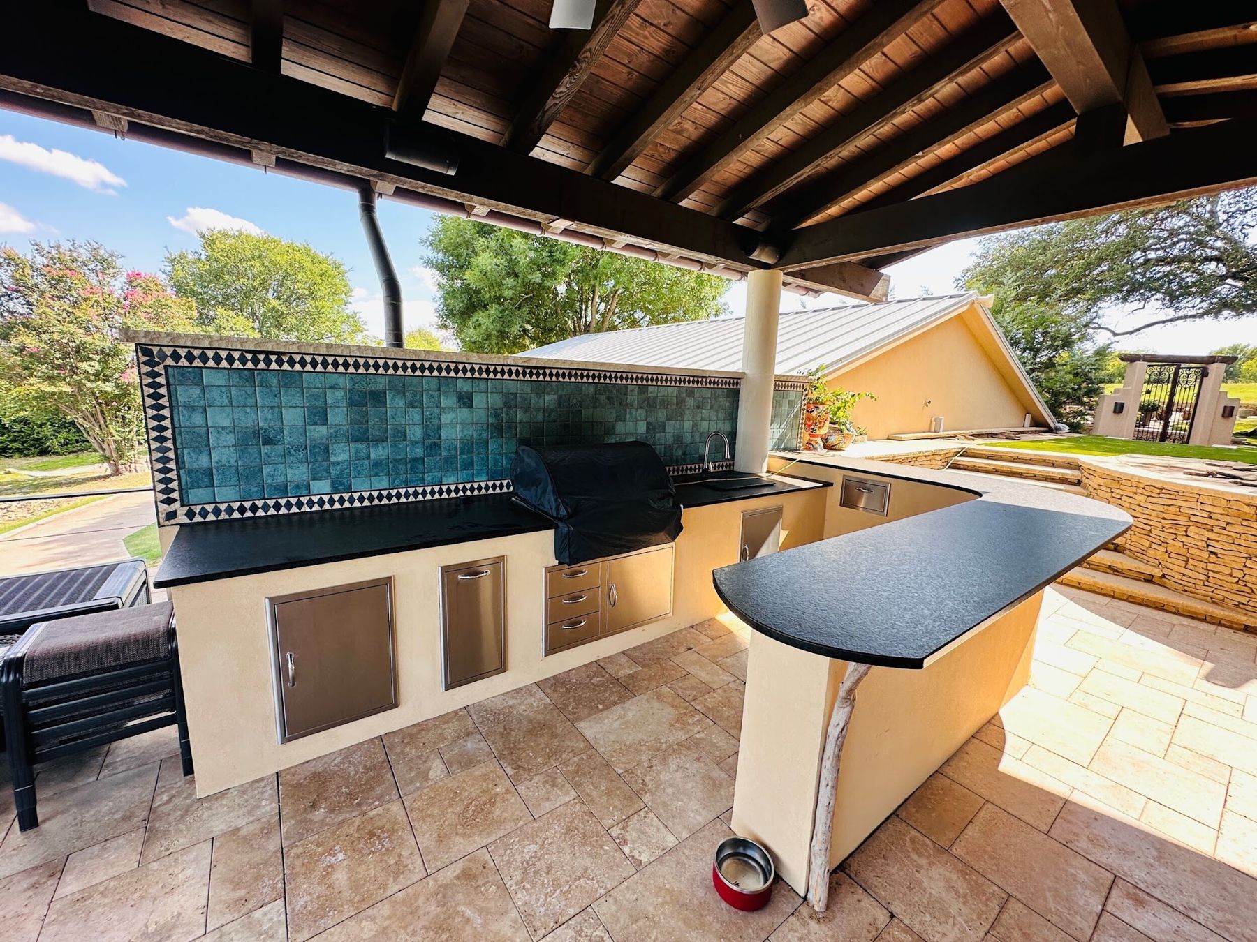 Kitchen bar with teal tile backsplash and curved black countertop