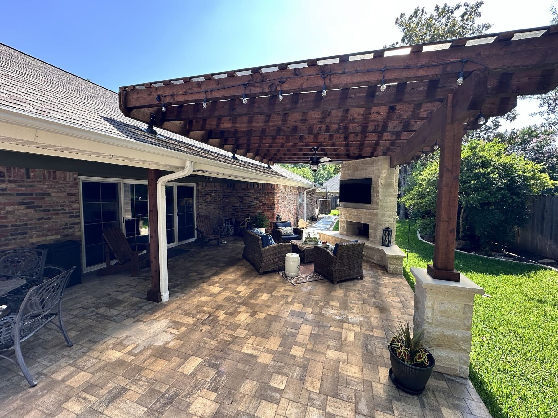 Stained pergola over a paver patio with fireplace
